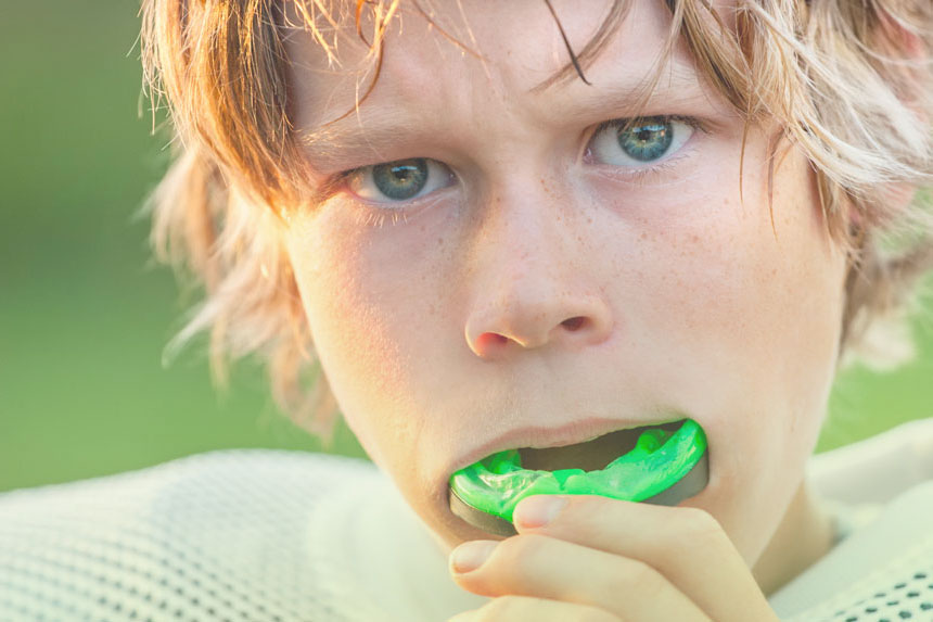 A young boy putting on a sports mouth guard before heading out to play, protecting his teeth during athletic activities