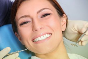 Smiling woman receiving professional teeth cleaning from a dentist using dental instruments.