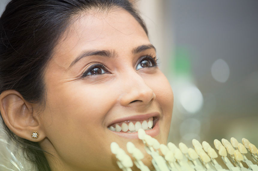 Close-up of a Calgary dentist matching a veneer shade tray to a woman’s teeth during a cosmetic dentistry consultation