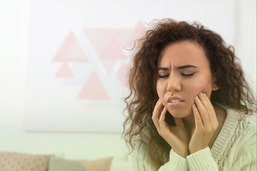 Woman holding her cheeks in pain due to wisdom tooth problems, seeking removal treatment at Dr. Brent MacDonald’s Calgary dental clinic.