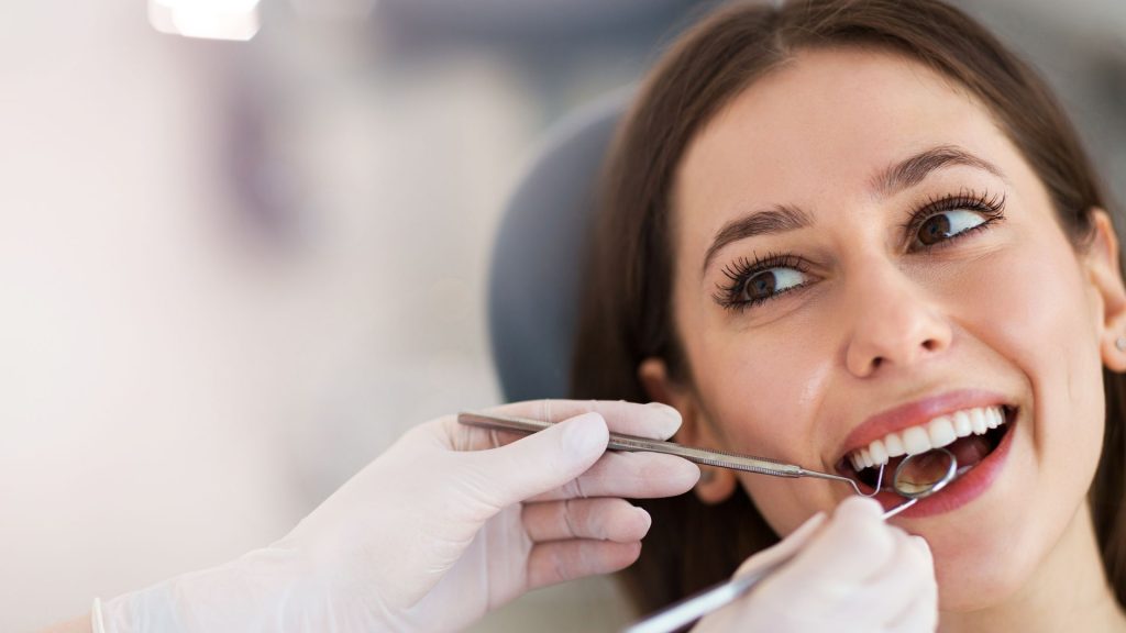 Woman receiving a dental check-up with mirror and probe during a cavity examination before a filling procedure.