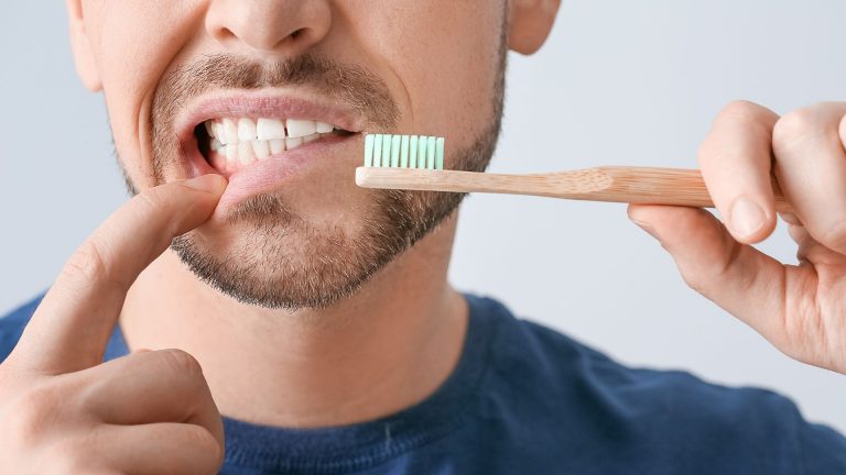 Man pointing to his gums while holding a toothbrush, wondering when he can brush after wisdom tooth extraction.