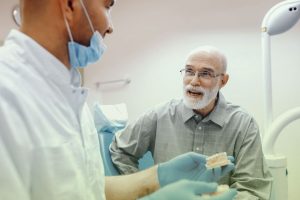A Calgary dentist holding a model of dental bridges while explaining the treatment process to an elderly patient during a consultation.