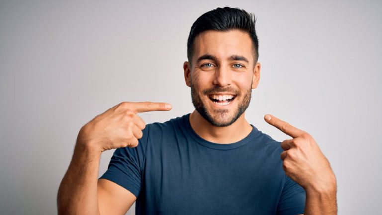 Smiling man pointing at his bright white teeth after home teeth whitening treatment, recommended by Dr. Brent MacDonald’s Calgary dental clinic.