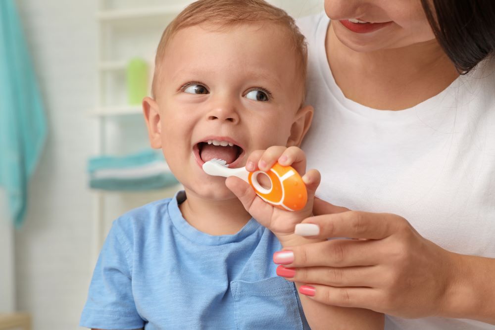 Happy kid smiling while her mother teaches her to brush teeth, encouraging healthy oral care