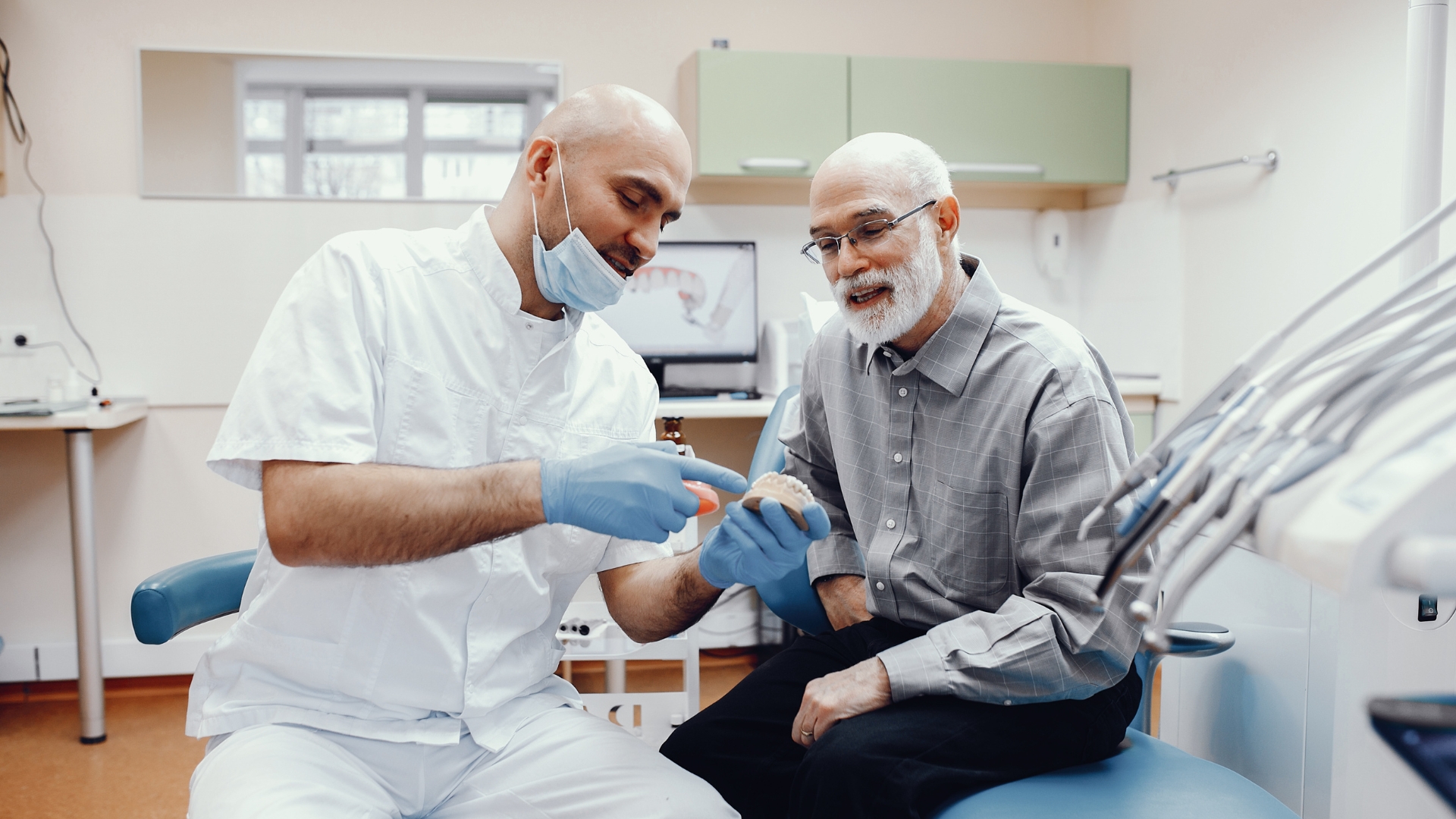 A Calgary dentist holding a model of dental bridges while explaining the treatment process to an elderly patient during a consultation.