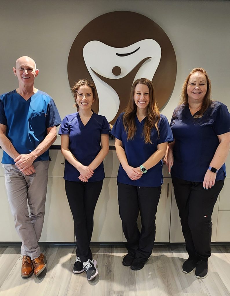 Dental team of Dr Brent MacDonald standing behind clinic logo in NE Calgary